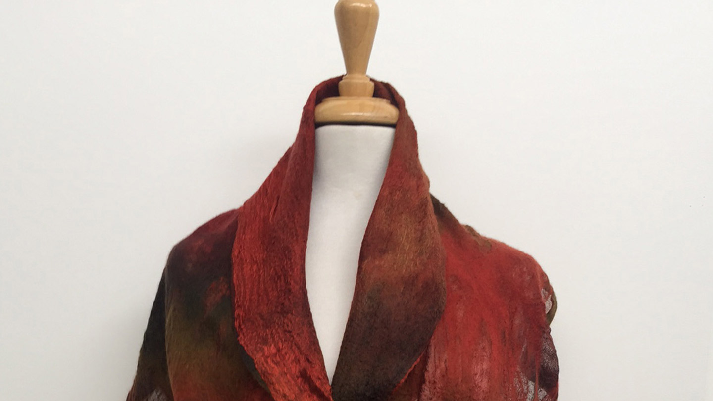 A flowing scarf in rusty red and brown tones wrapped around a mannequin