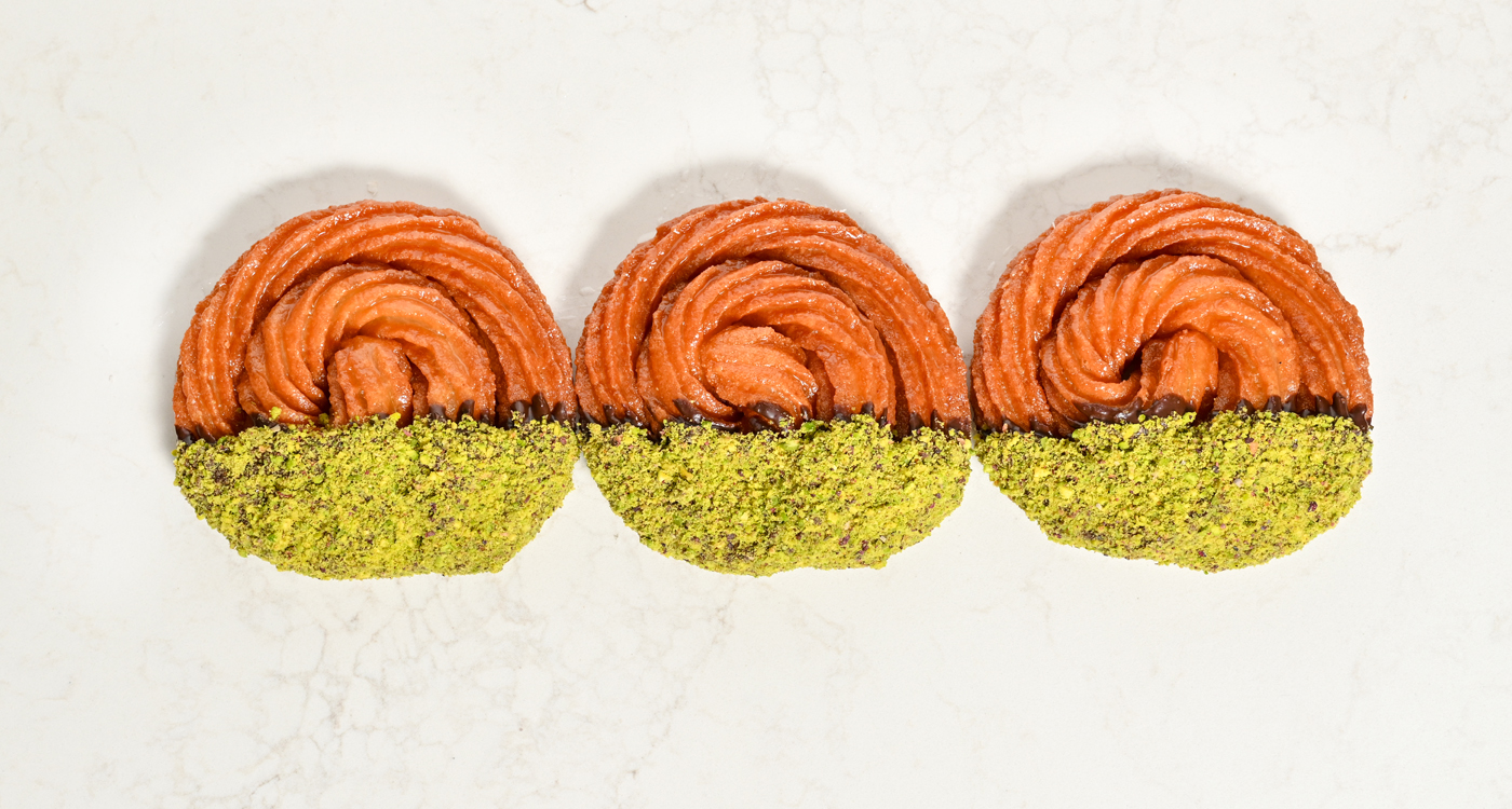 A flat lay style image of three Turkish donuts in a spiral shape, with half covered in a pistachio crumb. 