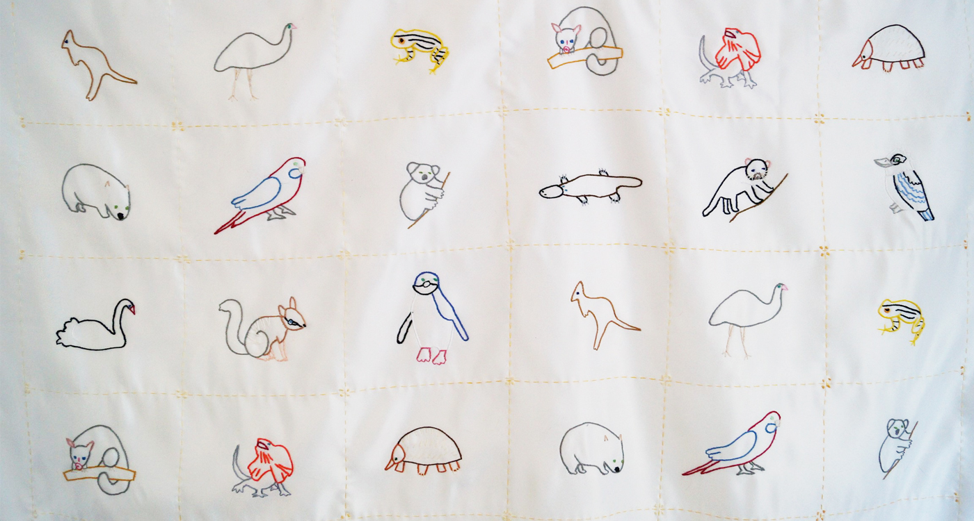 A white blanket with embroidered Australian animals in small squares. 