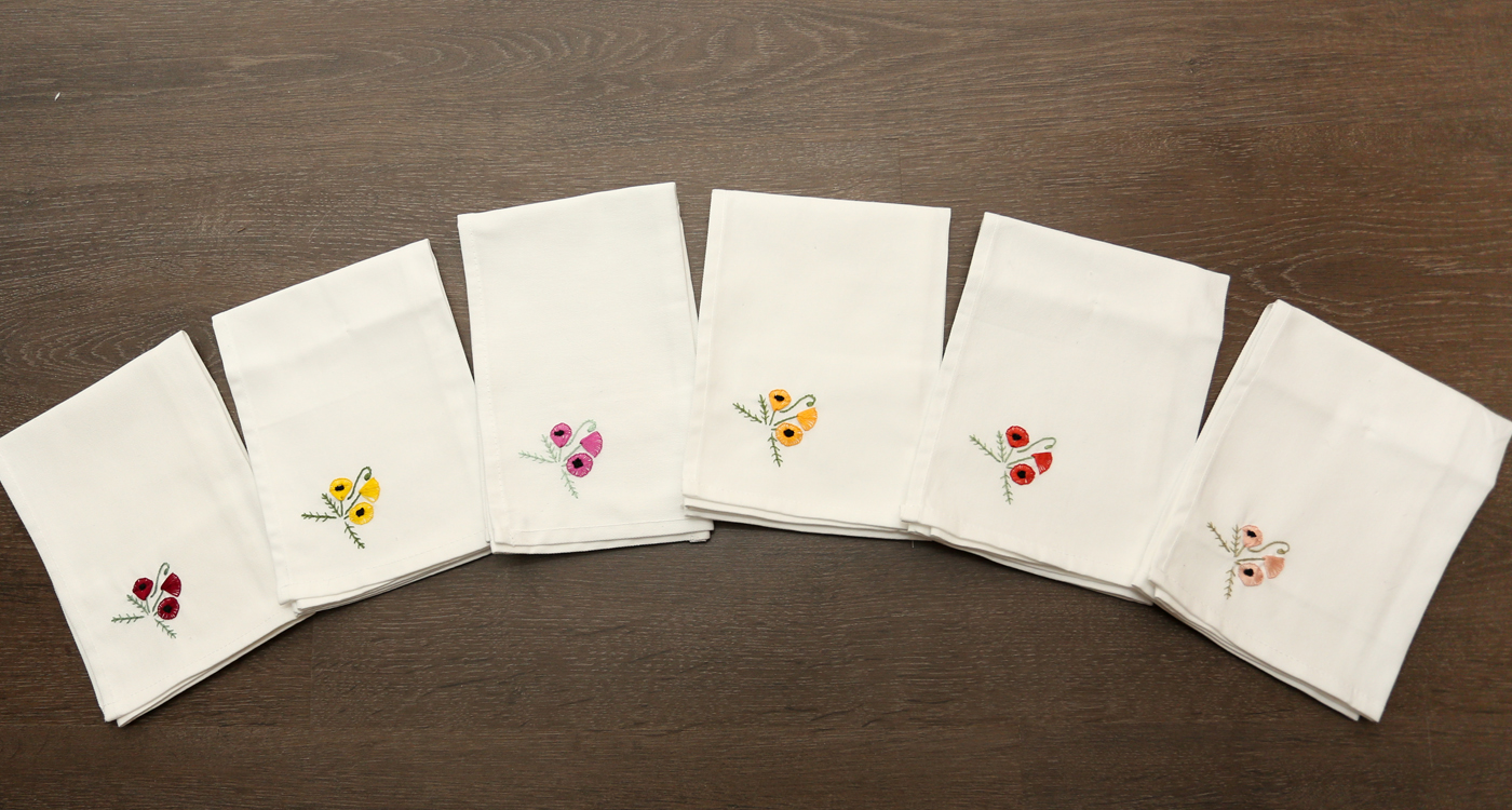 A top down image of six white handkerchiefs with embroidered flowers in one corner.