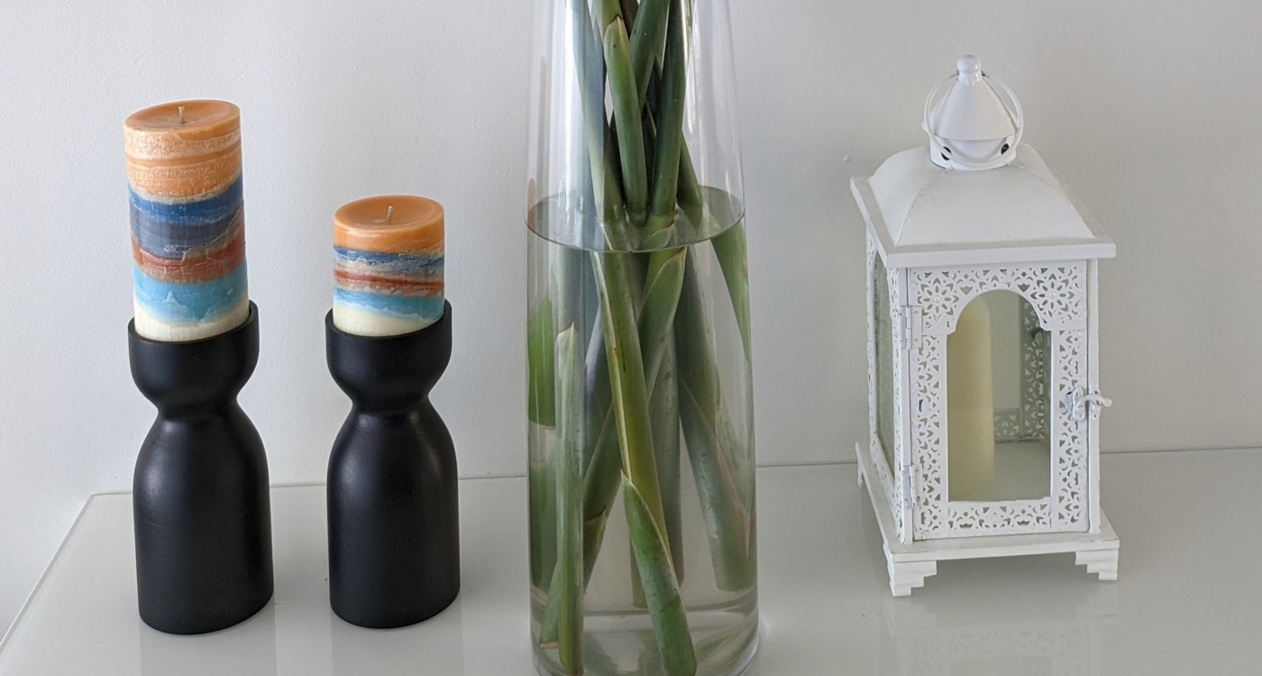 A collection of items on a counter, including, three candles and a vase filled with water and the bottom of stems. 